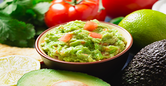 A bowl of guacemole surrounded by tomatoes and avocados